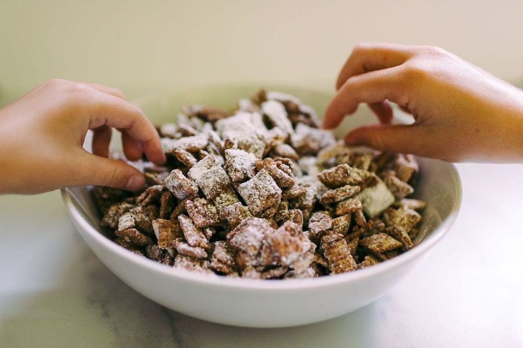 Children's hands reaching into a bowl of muddy buddies snack mix