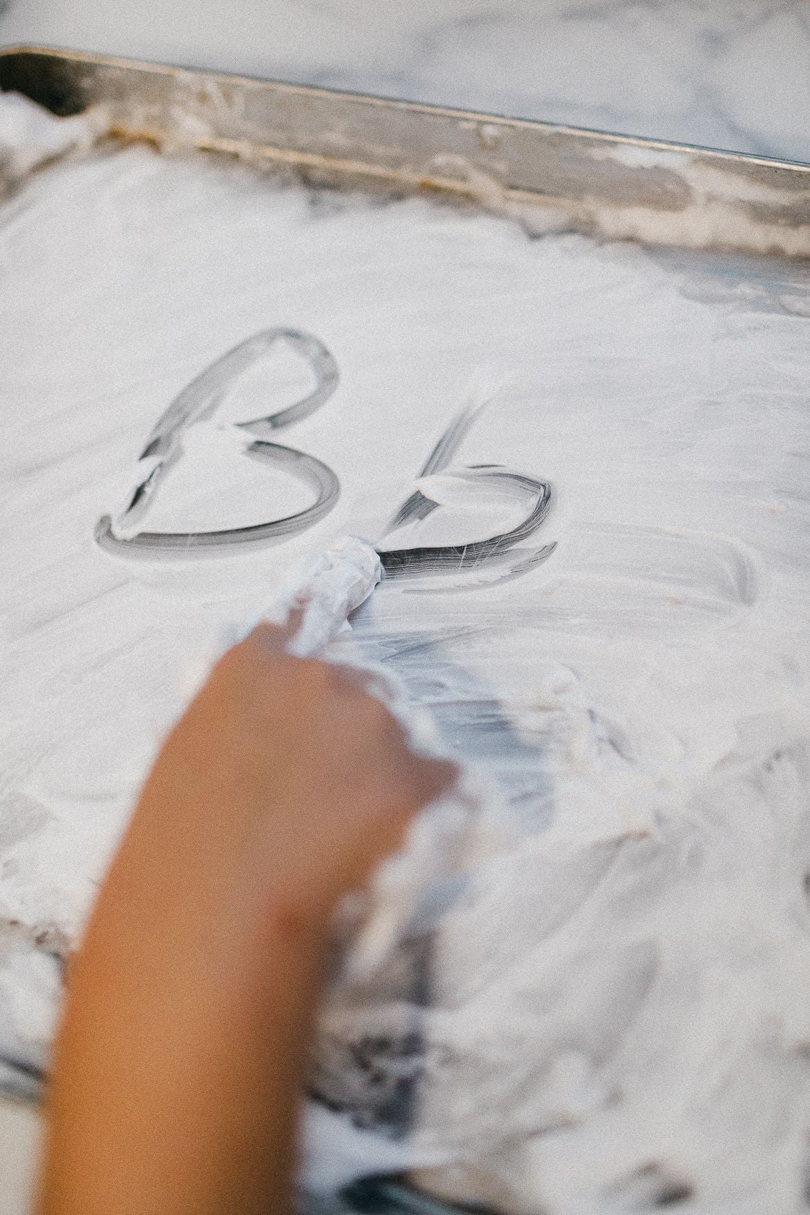 A childs hand writing letters in shaving cream