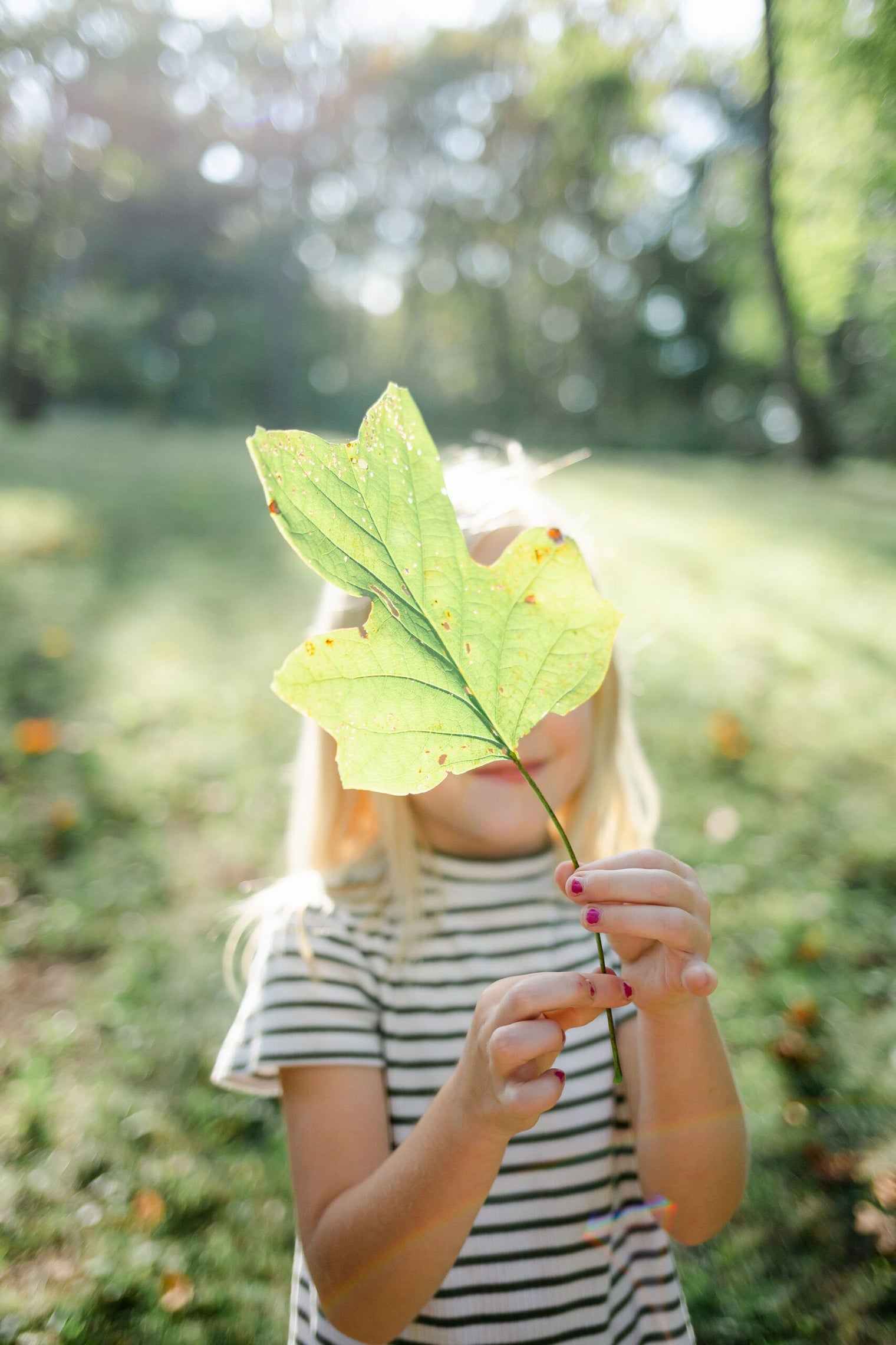 Girl holding leaf in front of her face outside