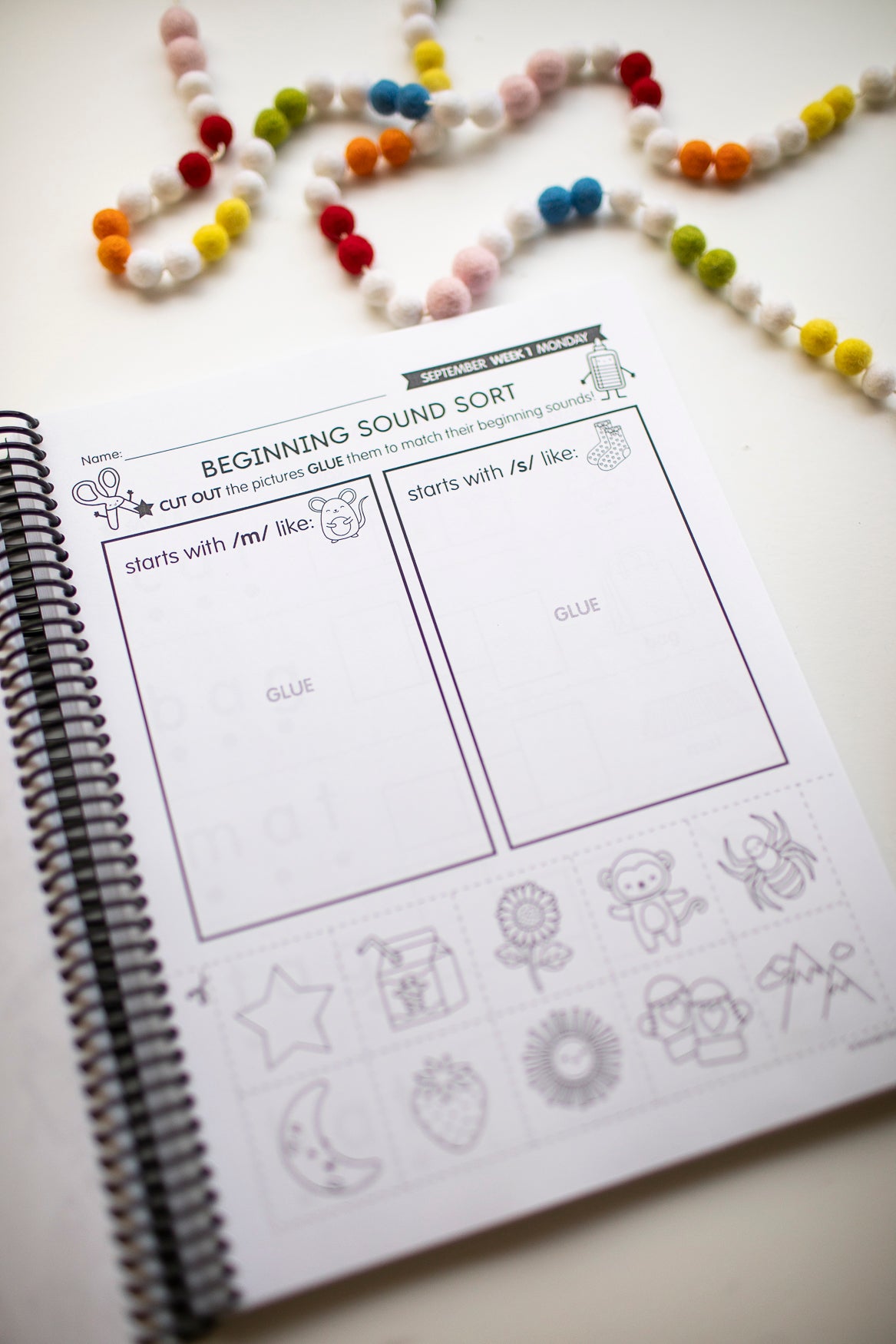 Educational worksheet on a spiral-bound book with bead decorations in the background