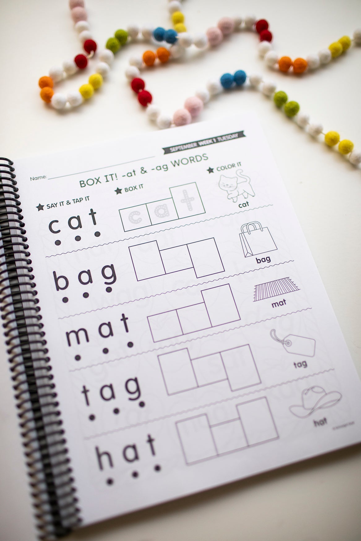 Educational worksheet on a spiral-bound book with bead necklace in the background